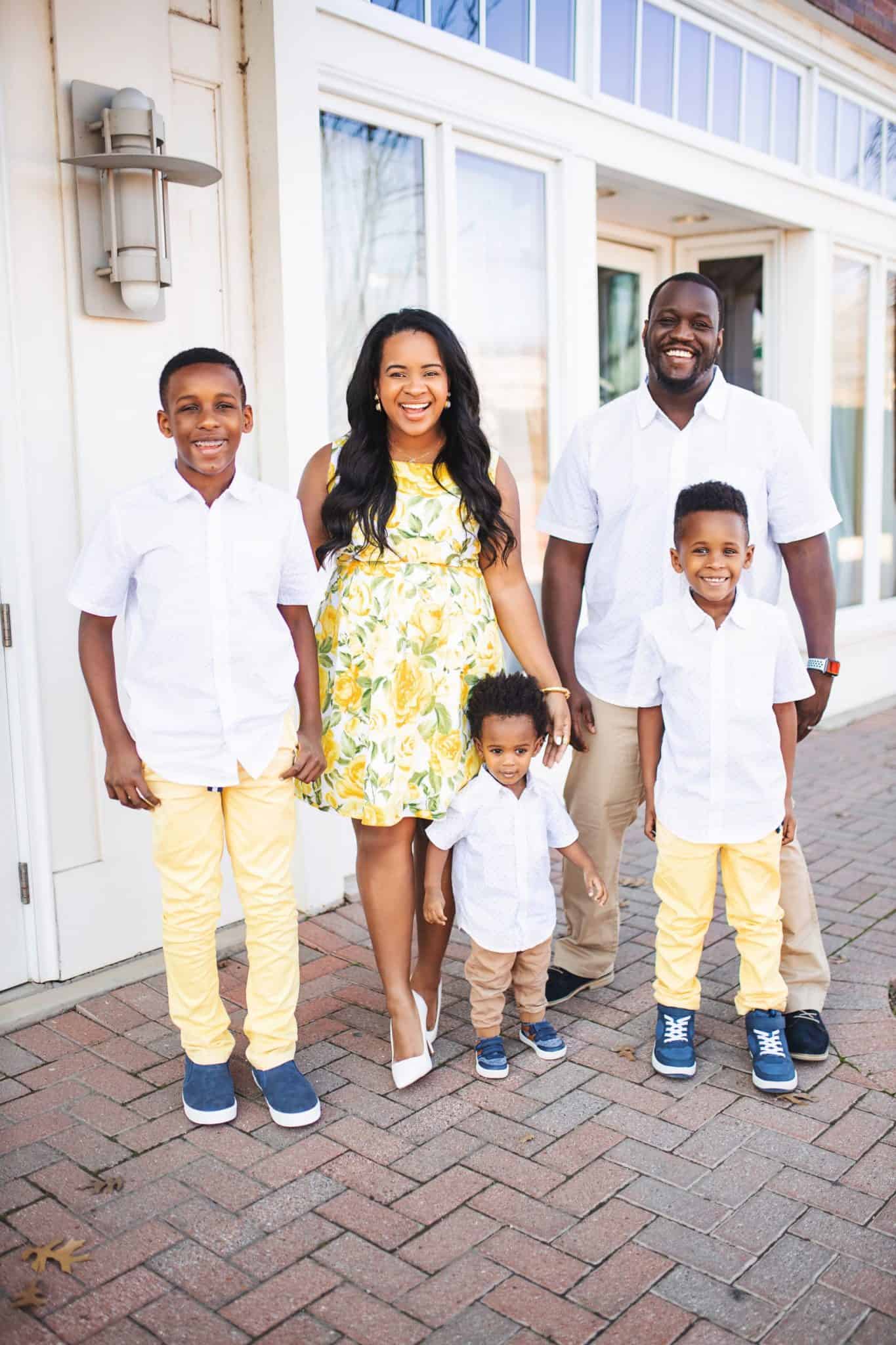 Matching Family Outfits for Spring by popular Dallas fashion blog, Glamorous Versatility: image of a family standing together outside and wearing Red Dress Upgrade Your Style White Crocodile Heels, The Children's Place Womens Mommy And Me Floral Matching Pleated Dress, The Children's Place Baby And Toddler Boys Dad And Me Print Poplin Matching Button Down Shirt, and The Children's Place Baby And Toddler Boys Belted Matching Chino Pants.