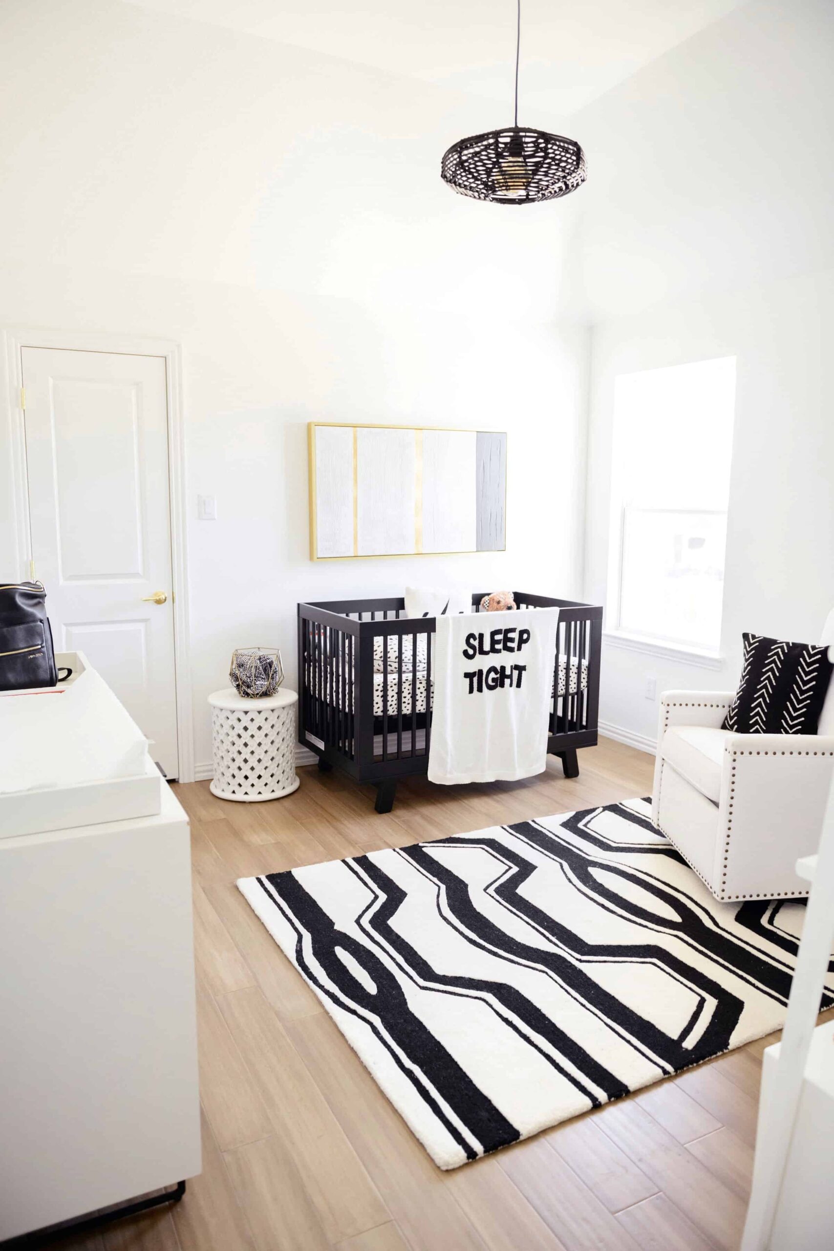 Wood Floor Installation by popular Dallas life and style blog, Glamorous Versatility: image of a boys room with light wood floors, black light fixture, black crib, black and white rug, white dresser, and white glider chair. 