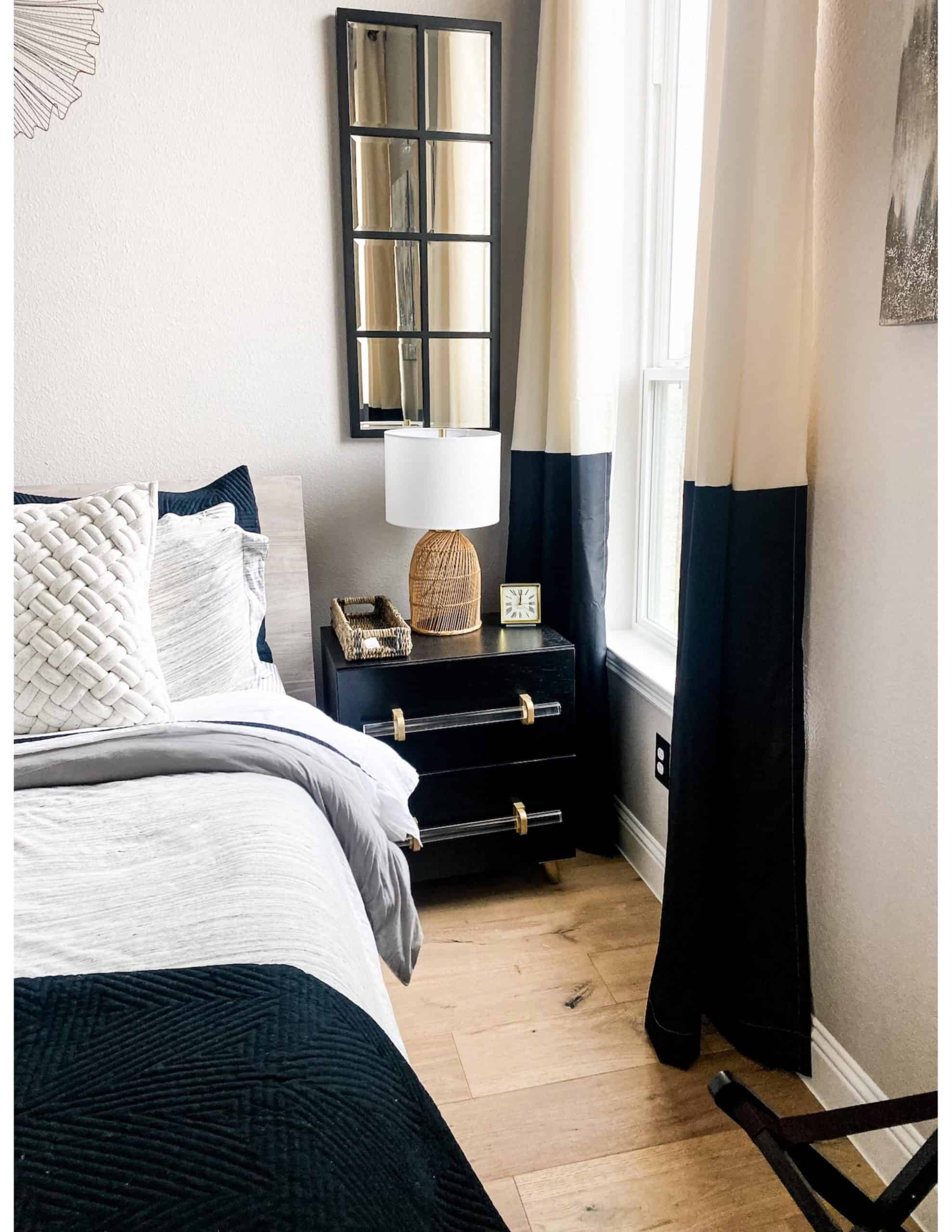Modern Guest Bedroom by popular Dallas life and style blog, Glamorous Versatility: image of a guest bedroom decorated with black dressers, black and white striped bench, queen size bed with black white, and blue bedding, black and white drapes, modern brass and glass light fixture, woven cream area rug, wicker lamps, and black frame mirrors. 